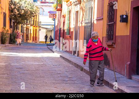 An old, Mexican woman walks down the street using a cane to keep her balance. San Miguel de Allende, Guanajuato, Mexico Stock Photo