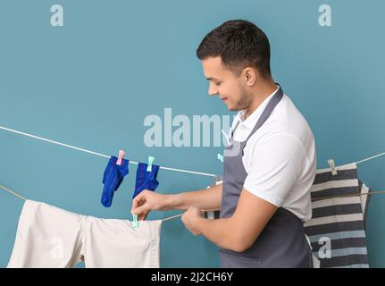 Young man hanging clean laundry with clothespin on blue background Stock Photo