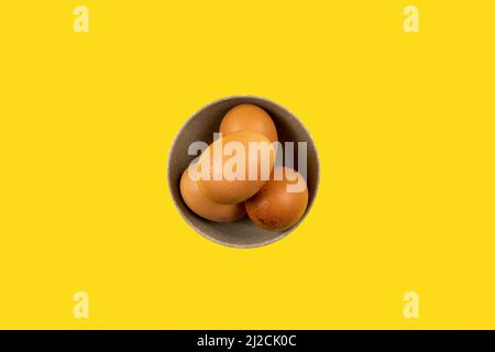 Top view of a ceramic bowl filled with fresh chicken eggs on a yellow background Stock Photo