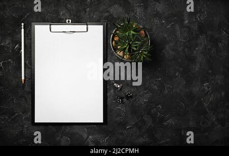 Blank clipboard, pencil, succulent plant and clips on black plaster background. Top view with copy space. Flat lay. Stock Photo