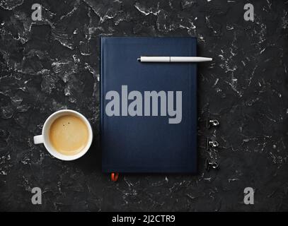 Blank notepad, pen, coffee cup and clips on black plaster background. Top view. Flat lay. Stock Photo