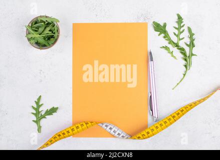 Planning a diet, arugula salad and tailor tape measure around the empty paper, healthy food and lifestyle, loosing weight Stock Photo