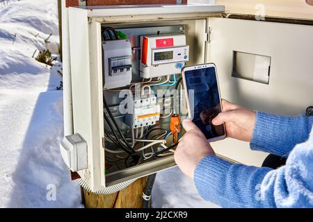 Taking readings from external electric meter and making photo using smartphone outside in winter. Stock Photo