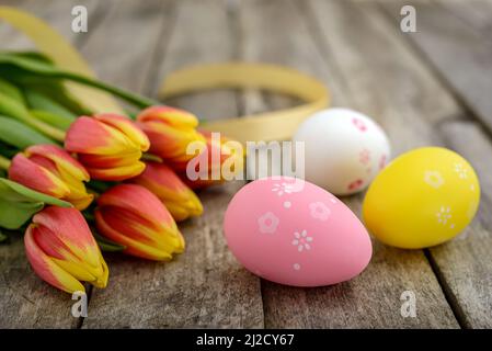 A group of colorful decorated Easter eggs and a bouquet of tulips on a rustic wooden table. Easter concept. Stock Photo