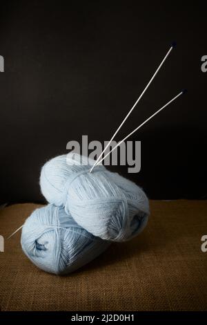 Some balls of blue yarn with the knitting needles stuck on them on a black background, copy space and side light Stock Photo