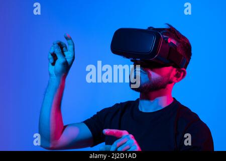 Man in virtual 3d glasses working on a project in a studio in neon light. Man playing video games with a friends at home using vr goggles. Stock Photo