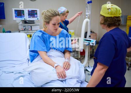 Preparing the final stages before surgery. Shot of a young pregnant woman sitting on her hospital bed and looking thoughtful with nurses in the Stock Photo