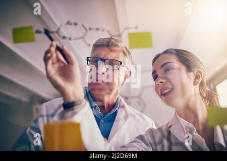 This makes a whole lot of sense. Shot of two focused scientists working together solving equations on a glass wall in a laboratory. Stock Photo