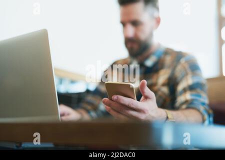 Take your wireless devices wherever you go. Shot of a young man using his cellphone and laptop while sitting in a cafe. Stock Photo
