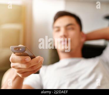 Seeking the sports channel. Shot of a young man using a remote control to change the channel on his television while he lies on the couch. Stock Photo