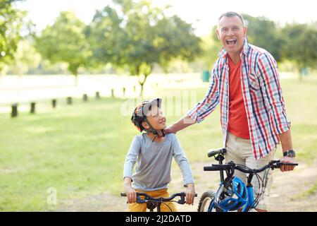 Hes a better rider than me now. Portrait of a father and son riding bicycles in a park. Stock Photo