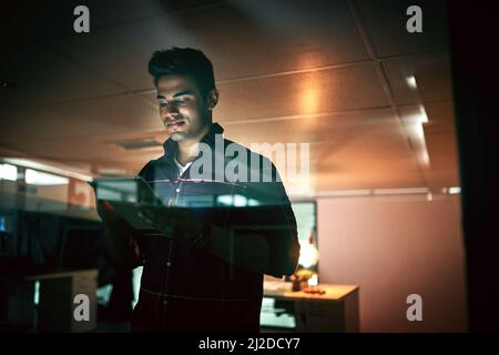 All nighters are nothing for a get it done guy. Shot of a young businessman using a digital tablet during a late night at work. Stock Photo