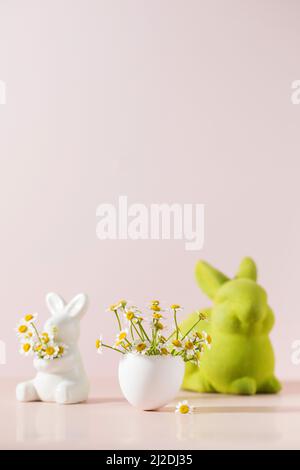 Easter concept. Bouquet of chamomiles in an eggshell on a pink background with easter bunnies. Stock Photo