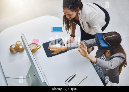 This is unreal. High angle shot of a young businesswoman using a VR headset while being assisted by a female colleague. Stock Photo