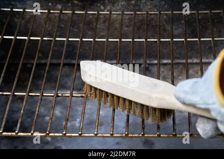 Wooden wire brush cleans dirty barbecue grill rust. Leather protection gloves. Stock Photo