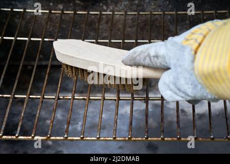 Wooden wire brush cleans dirty barbecue grill rust. Leather protection gloves. Stock Photo