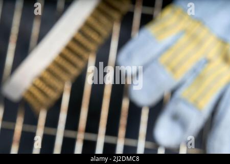 Dirty grill grate with cleaning tool. Leather glove and wooden wire brush on empty barbecue grill. Defocused. Stock Photo