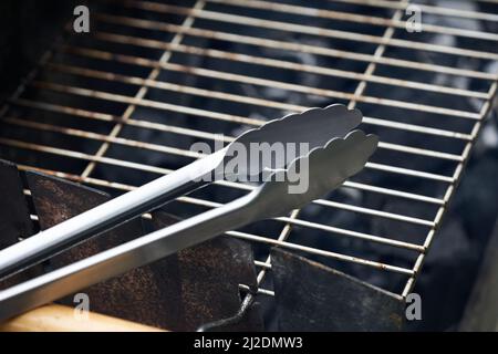 Stainless steel grill tongs on a dirty grill rust. Wooden handle blurred in the foreground. Stock Photo