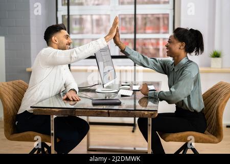 Businessman And Businesswoman Sitting On Chair Giving High Five In Front Of Computer At Workplace Stock Photo