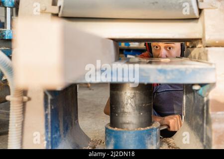 Attentive woodworker using thicknesser machine to trim wooden board Stock Photo