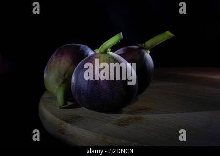 Three figs on a cutting board in a black background, with a rim light, still life photography Stock Photo