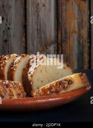 Slices of sweet bread with pieces of walnuts on top, over a mud or clay mexican plate and awooden background Stock Photo