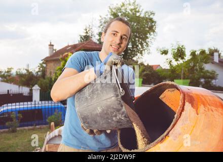 Man add a bucket of sand to cement mixer doing DIY work at home Stock Photo