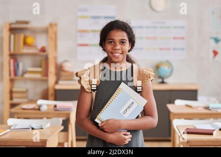 Waist up portrait of smiling African-American girl in school looking at camera while standing in classroom, copy space Stock Photo