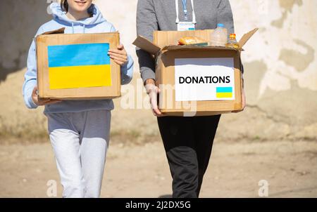 Young volunteers taking a box of food from their car for the Ukrainian refugee with painted flag on the boxes. Stock Photo