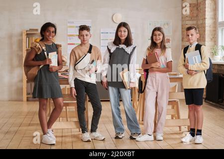Full length portrait of diverse group of kids in school looking at camera while standing in classroom with backpacks Stock Photo