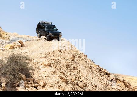 off road SUV jeep-type vehicle maneuvering down a steep descent on a barren desert mountain with a clear blue sky background Stock Photo