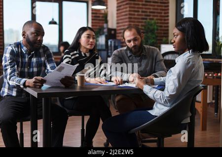 Employers sitting at desk table during interview meeting in startup company office. Managers analyzing cv resume hiring candidate for human resources job while sitting in meeting room. Stock Photo