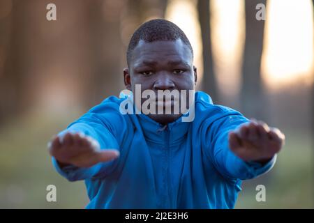 Portrait of a young black man in sportswear doing squats outdoor early in the morning. Stock Photo