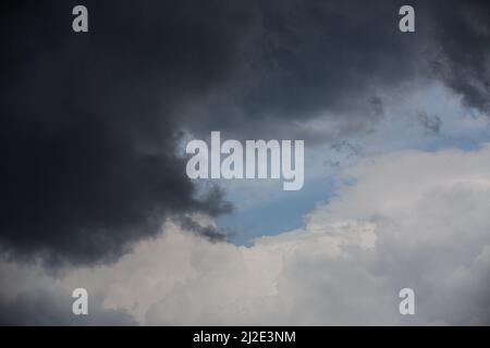 A white cloud collides with a dark thundercloud against a background of blue sky Stock Photo