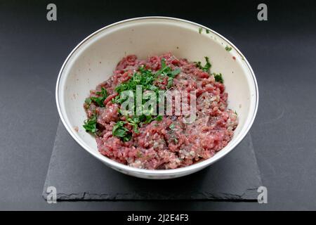 Homemade minced meat for cutlets with parsley in a bowl for cooking on a dark background on the table Stock Photo