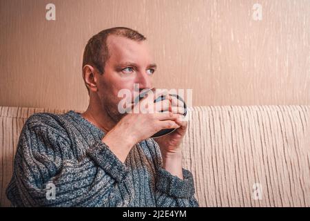 Portrait of a man drinking from a black cup. White man sitting on the couch and drinking from a cup, close-up Stock Photo