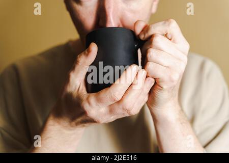 Portrait of a man drinking coffee from a black cup, White man drinking from a cup, close-up Stock Photo