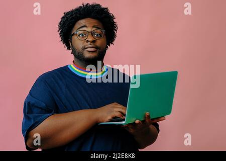 young african american man posing with laptop in the studio over pink background male model Stock Photo