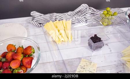Step by step. Arranging cheese platter with fresh fruits, gourmet cheese, and crackers. Stock Photo