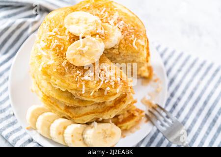 Eating freshly baked coconut banana pancakes garnished with sliced bananas and toasted coconut. Stock Photo