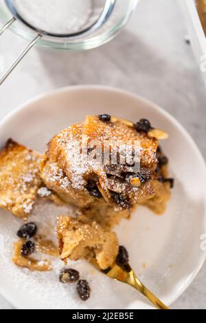 Serving freshly baked bread pudding with raising and almond slivers in a white casserole dish. Stock Photo