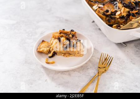 Serving freshly baked bread pudding with raising and almond slivers in a white casserole dish. Stock Photo