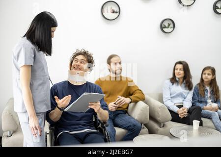 Medical worker communicates with guy in wheelchair at the clinic reception Stock Photo