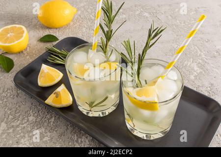 two glasses of citrus fruit vitamin water on a dark ceramic tray with lemon slices and rosemary. detox water Stock Photo
