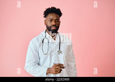 Thoughtful male surgeon holding pen while looking at camera against pink background Stock Photo