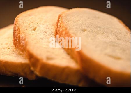 slices of white bread close up on a black background. rough dappled textured surface chopped pieces loaf of natural organic food with holes Stock Photo