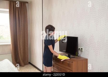 Wife dusting TV screen while cleaning house., Stock Photo