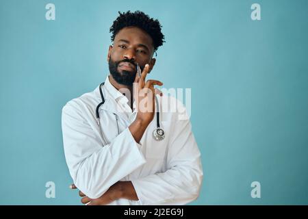 Thoughtful male surgeon holding pen while looking at camera against turquoise background Stock Photo