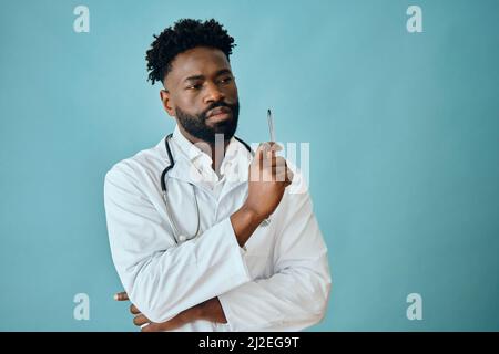 Thoughtful male surgeon holding pen while looking away against turquoise background Stock Photo