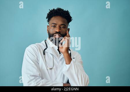 Portrait of thoughtful male healthcare worker with hand on chin against turquoise background Stock Photo